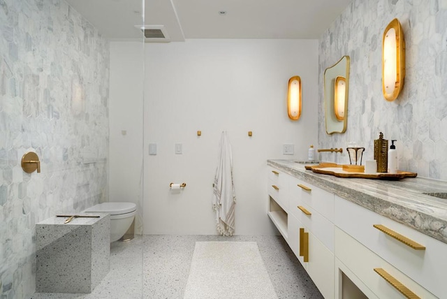 bathroom with vanity, toilet, and tile walls