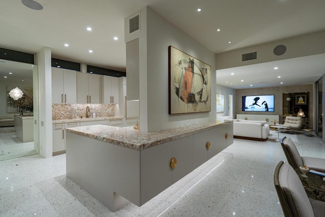 kitchen with sink, white cabinetry, a center island, tasteful backsplash, and light stone countertops