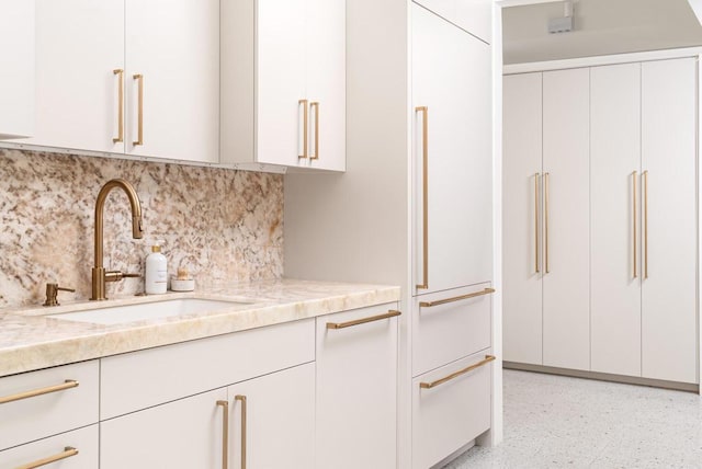 kitchen with tasteful backsplash, sink, light stone counters, and white cabinets