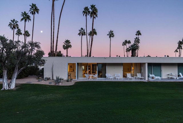 back house at dusk with a yard and a patio area