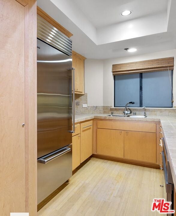 kitchen with light brown cabinetry, sink, light hardwood / wood-style floors, and stainless steel built in fridge