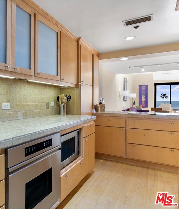 kitchen with tile countertops, light brown cabinetry, decorative backsplash, light hardwood / wood-style floors, and stainless steel appliances