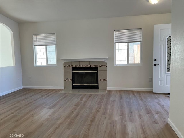 unfurnished living room with a tiled fireplace, a wealth of natural light, and light hardwood / wood-style flooring