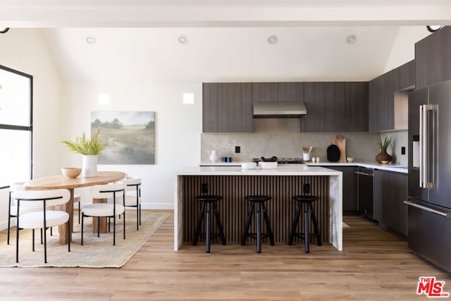 kitchen featuring lofted ceiling, a breakfast bar area, high quality fridge, light hardwood / wood-style floors, and backsplash