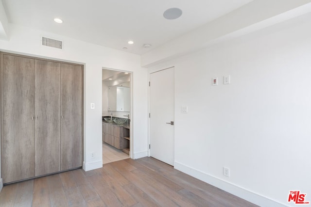 unfurnished bedroom with ensuite bathroom, sink, a closet, and light wood-type flooring