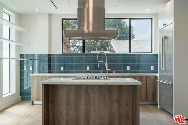 kitchen with island range hood, stainless steel appliances, sink, and light hardwood / wood-style flooring