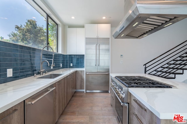 kitchen featuring sink, white cabinetry, range hood, light stone counters, and premium appliances