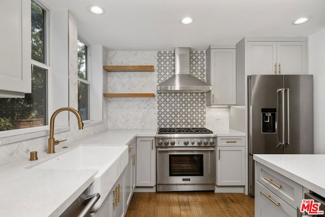 kitchen with tasteful backsplash, sink, premium appliances, wall chimney range hood, and light wood-type flooring