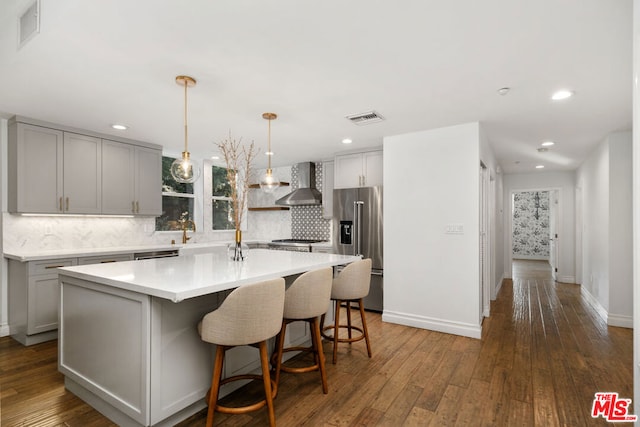 kitchen with wall chimney exhaust hood, a center island with sink, dark hardwood / wood-style floors, stainless steel appliances, and backsplash