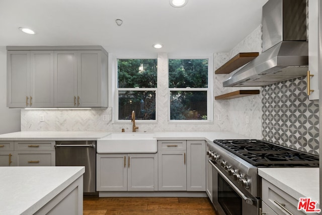 kitchen featuring sink, appliances with stainless steel finishes, tasteful backsplash, light hardwood / wood-style floors, and wall chimney exhaust hood