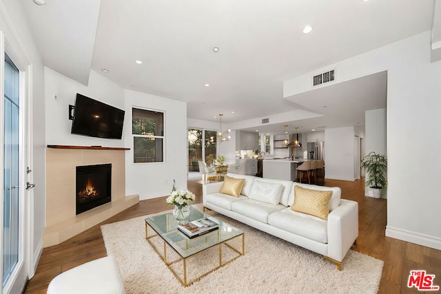 living room featuring hardwood / wood-style flooring, a tile fireplace, and a notable chandelier