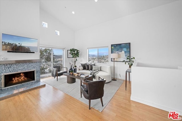 living room with a tile fireplace, high vaulted ceiling, and light hardwood / wood-style flooring