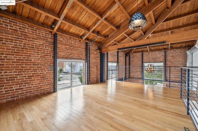 interior space with a high ceiling, brick wall, hardwood / wood-style floors, and beam ceiling