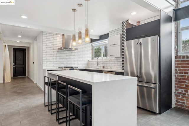 kitchen featuring a kitchen island, a kitchen bar, decorative light fixtures, high end refrigerator, and wall chimney exhaust hood