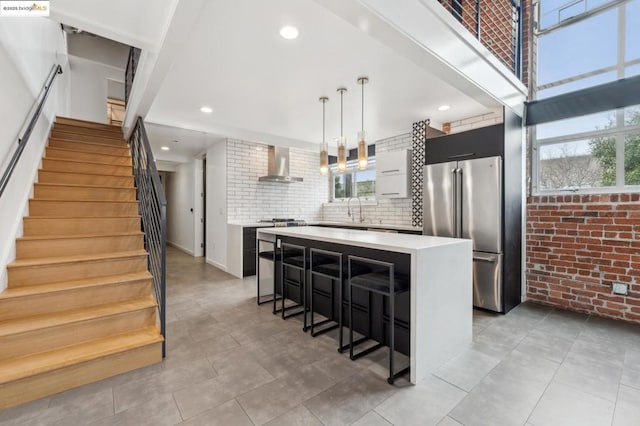 kitchen featuring wall chimney exhaust hood, high end fridge, a breakfast bar area, a center island, and pendant lighting