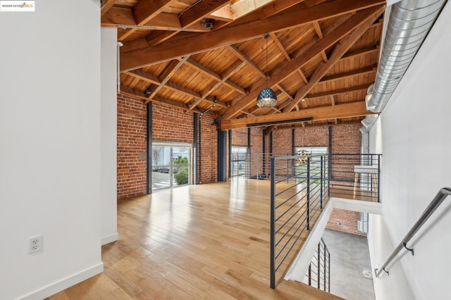 interior space with brick wall, a towering ceiling, beamed ceiling, wood-type flooring, and wooden ceiling