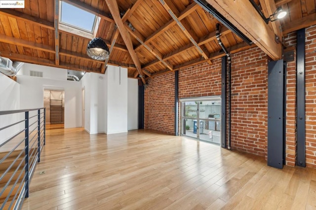 interior space with light hardwood / wood-style flooring, beam ceiling, a skylight, a high ceiling, and brick wall