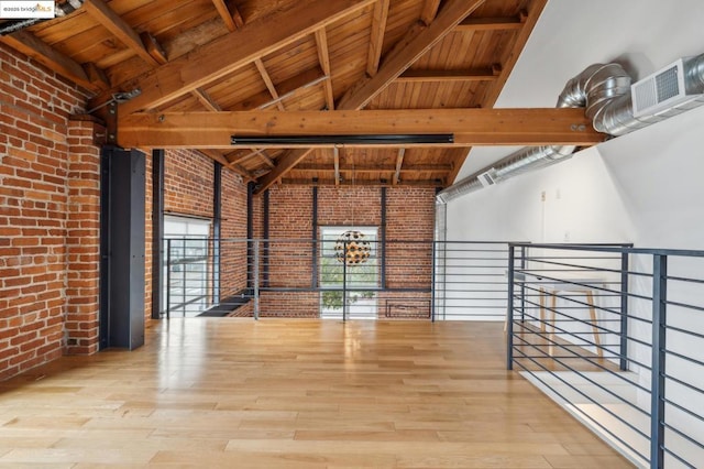 unfurnished living room with beam ceiling, high vaulted ceiling, hardwood / wood-style flooring, and brick wall