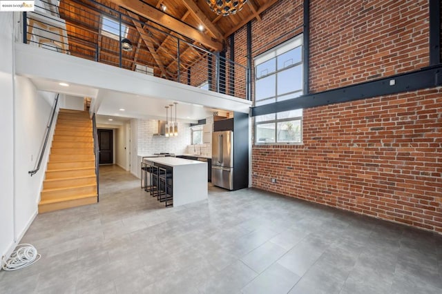 kitchen featuring pendant lighting, high end fridge, a kitchen bar, a high ceiling, and brick wall