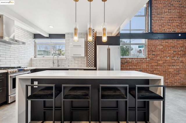 kitchen with sink, a breakfast bar area, a center island, stainless steel appliances, and wall chimney range hood