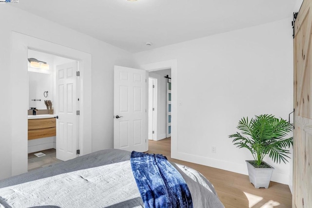 bedroom featuring ensuite bathroom, a barn door, and light wood-type flooring