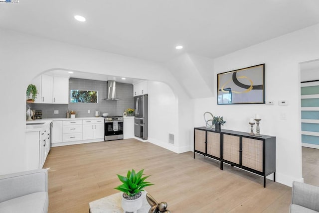 kitchen featuring appliances with stainless steel finishes, white cabinets, light hardwood / wood-style floors, decorative backsplash, and wall chimney range hood