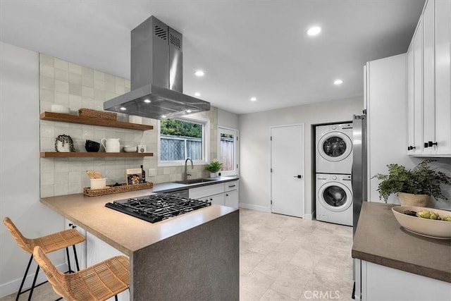 kitchen with stacked washing maching and dryer, white cabinetry, sink, a kitchen breakfast bar, and island exhaust hood