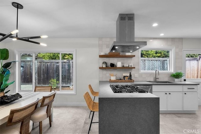 kitchen with sink, stainless steel gas cooktop, white cabinetry, island exhaust hood, and decorative backsplash