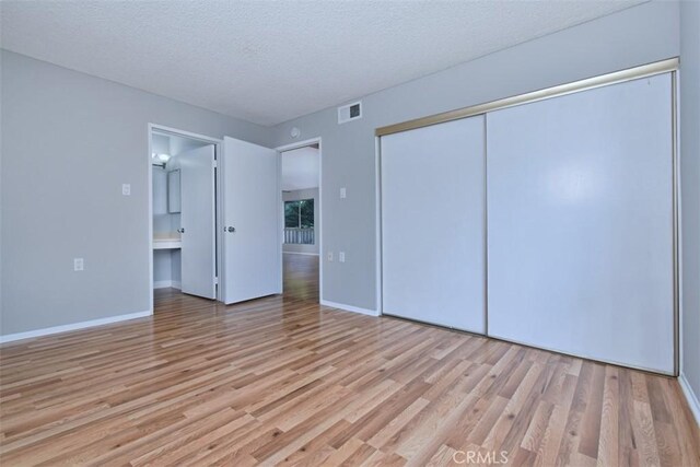 unfurnished bedroom featuring light hardwood / wood-style floors, a textured ceiling, and a closet