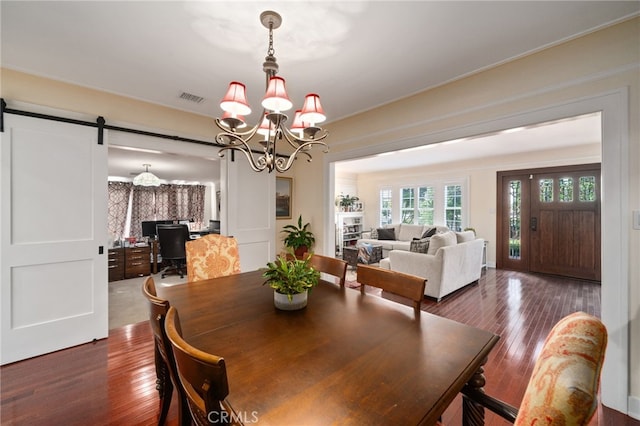 dining space with dark wood-type flooring, a barn door, and a chandelier