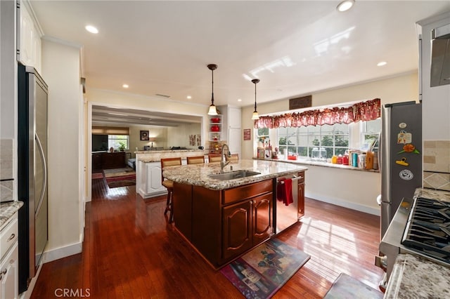 kitchen featuring sink, appliances with stainless steel finishes, an island with sink, white cabinets, and decorative light fixtures