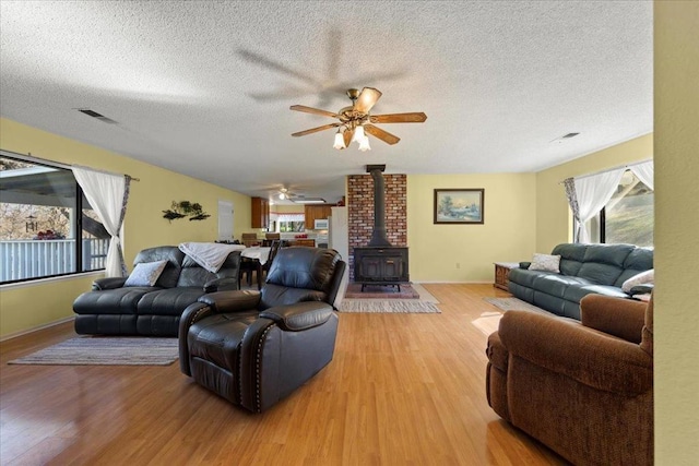 living room with ceiling fan, a wood stove, a textured ceiling, and light hardwood / wood-style floors