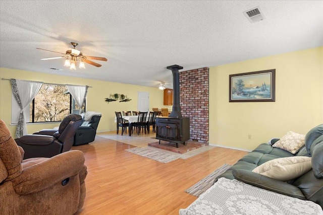 living room featuring ceiling fan, light wood-type flooring, a textured ceiling, and a wood stove