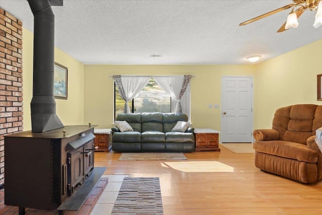 living room featuring ceiling fan, a wood stove, a textured ceiling, and light wood-type flooring