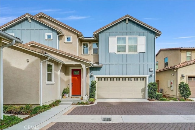 view of front of property with a garage, a tiled roof, decorative driveway, and board and batten siding