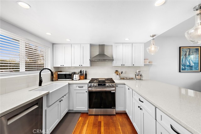 kitchen featuring pendant lighting, white cabinetry, decorative backsplash, stainless steel appliances, and wall chimney range hood