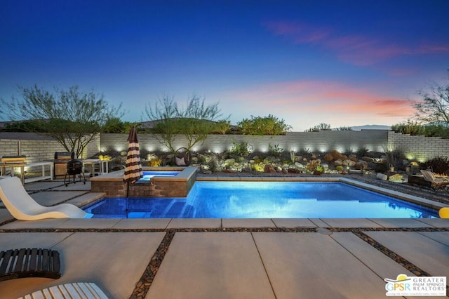 pool at dusk featuring an in ground hot tub, grilling area, and a patio area