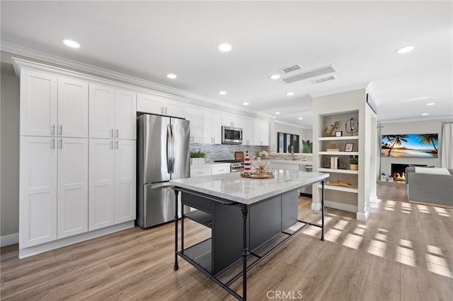 kitchen with white cabinetry, appliances with stainless steel finishes, a kitchen breakfast bar, a kitchen island, and light stone countertops