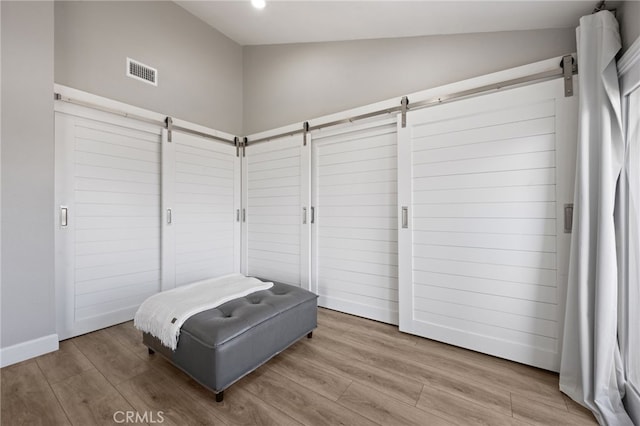 bedroom with vaulted ceiling, wood-type flooring, and a barn door