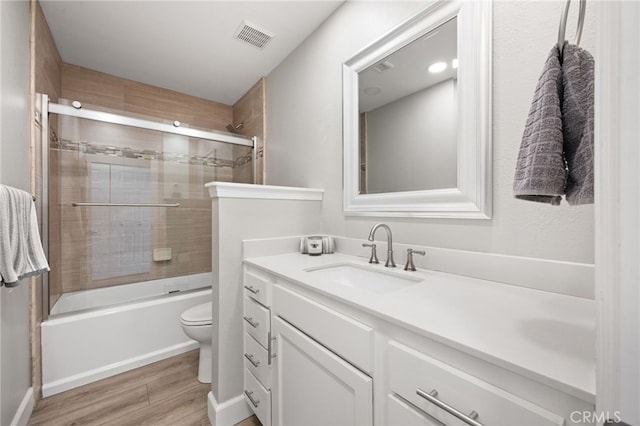 full bathroom featuring hardwood / wood-style flooring, vanity, bath / shower combo with glass door, and toilet