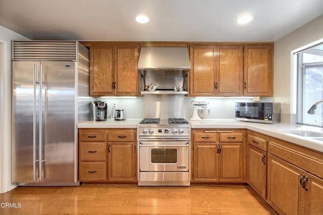 kitchen featuring wall chimney range hood, sink, high quality appliances, and light wood-type flooring