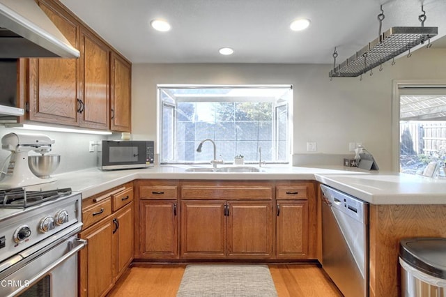 kitchen featuring wall chimney range hood, sink, appliances with stainless steel finishes, kitchen peninsula, and light wood-type flooring