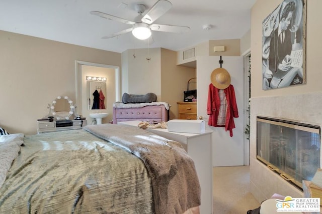 bedroom featuring ceiling fan, a tiled fireplace, and light colored carpet