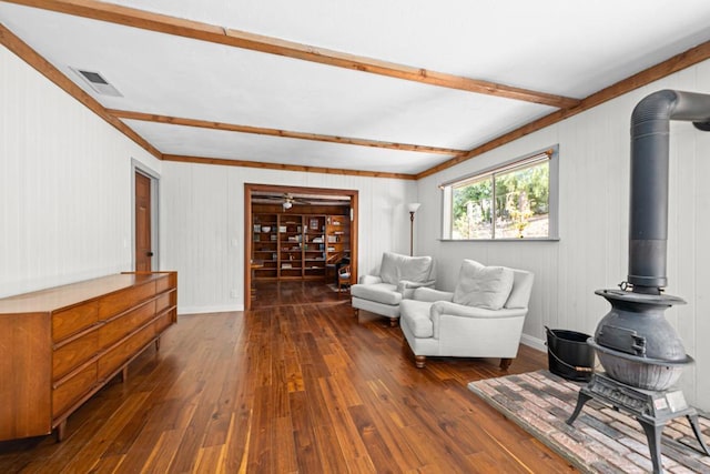 living room with beamed ceiling, a wood stove, dark wood-type flooring, and wood walls