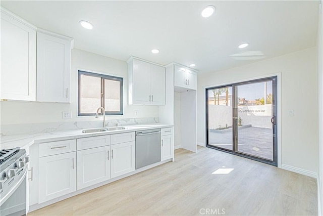 kitchen featuring appliances with stainless steel finishes, white cabinetry, sink, light stone countertops, and light wood-type flooring