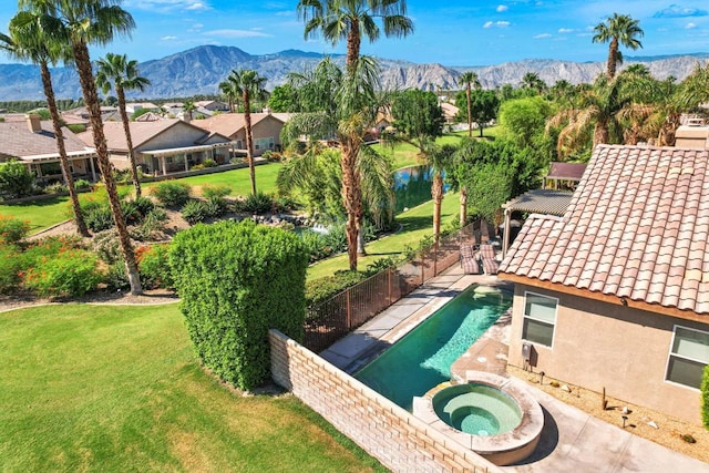 view of swimming pool with a mountain view, a lawn, and an in ground hot tub