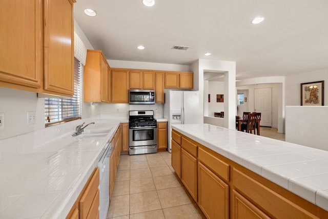 kitchen with stainless steel appliances, tile countertops, sink, and light tile patterned floors