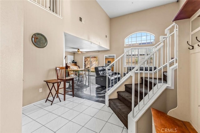 stairs with ceiling fan, a towering ceiling, and tile patterned flooring