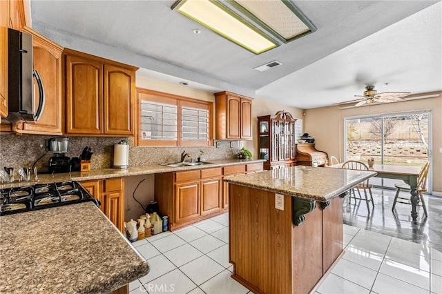 kitchen with decorative backsplash, sink, a kitchen island, and light tile patterned floors