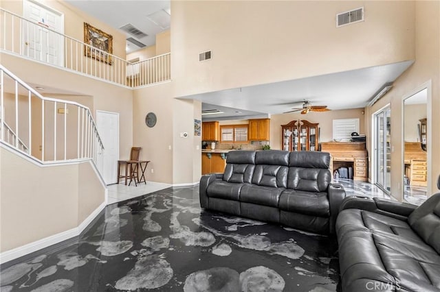 living room with a fireplace, ceiling fan, and a high ceiling